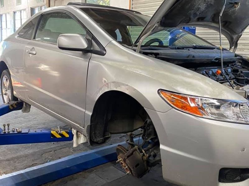 Silver sedan on a lift with front wheel removed, hood open in an auto repair shop