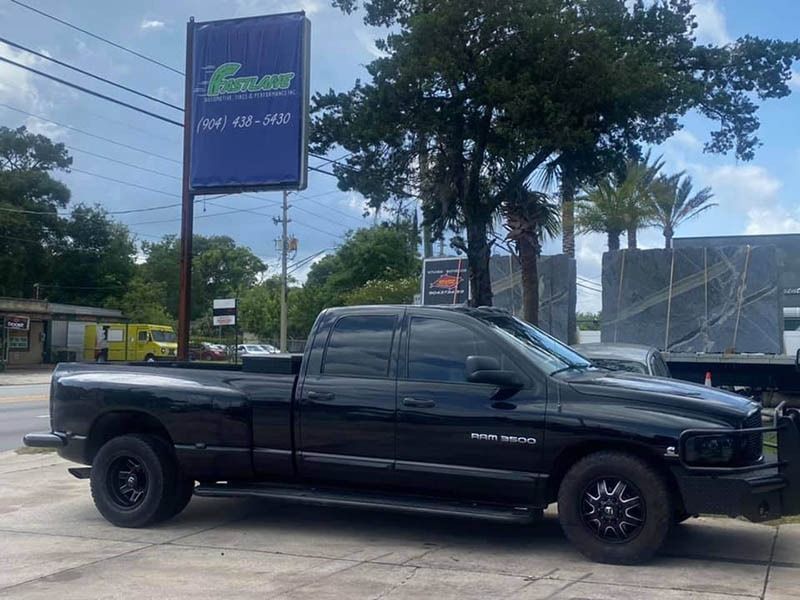 Black pickup truck parked beside a roadside sign and trees under a cloudy sky