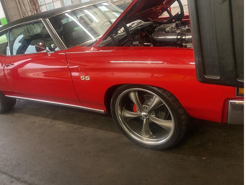 Red classic SS muscle car in a garage with its hood open, showing chrome wheels.