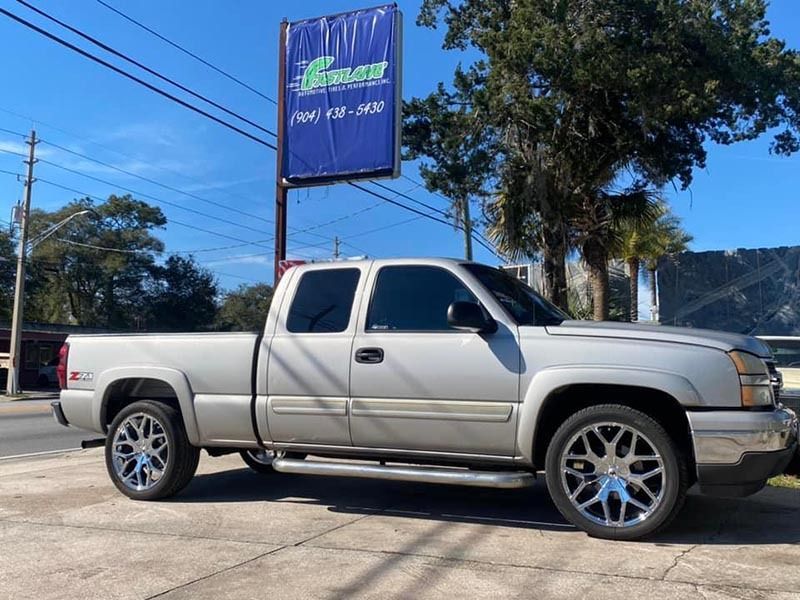 Silver pickup truck parked outdoors beside a roadside sign and palm trees.