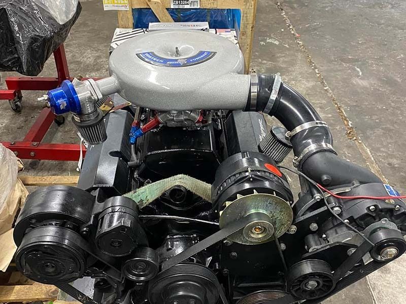 Compact car engine with gray intake piping and black pulleys on a workshop floor