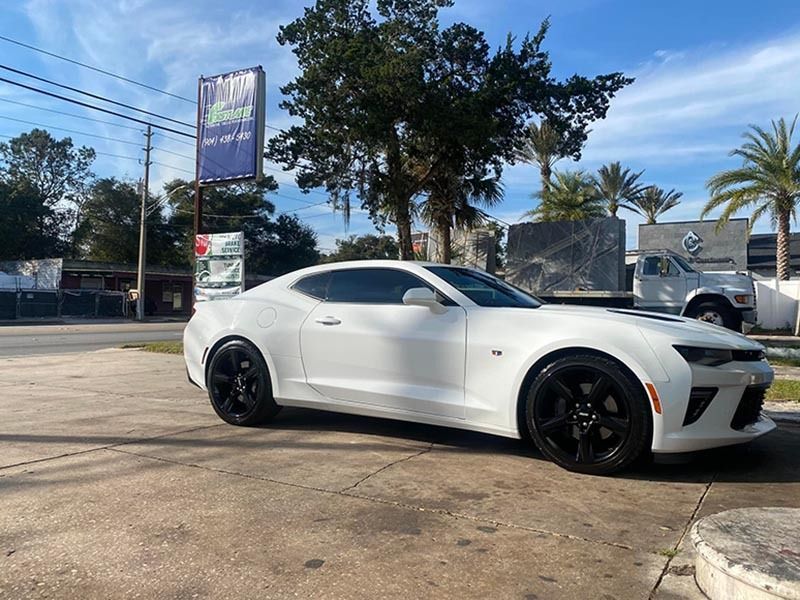 White sports coupe parked on a sunny street with palm trees in the background