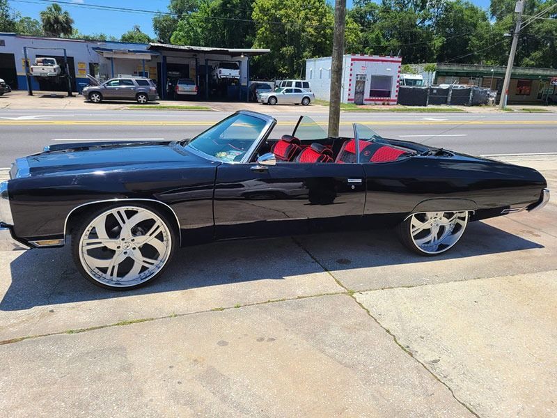 Black classic convertible with red interior parked on a sunny street, side view