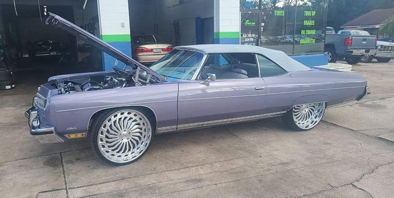 Lavender classic car with oversized chrome wheels parked in a garage.