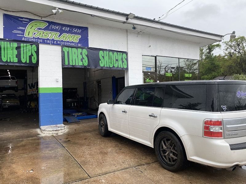 White SUV parked outside a tire and wheel shop with green signage and wet pavement