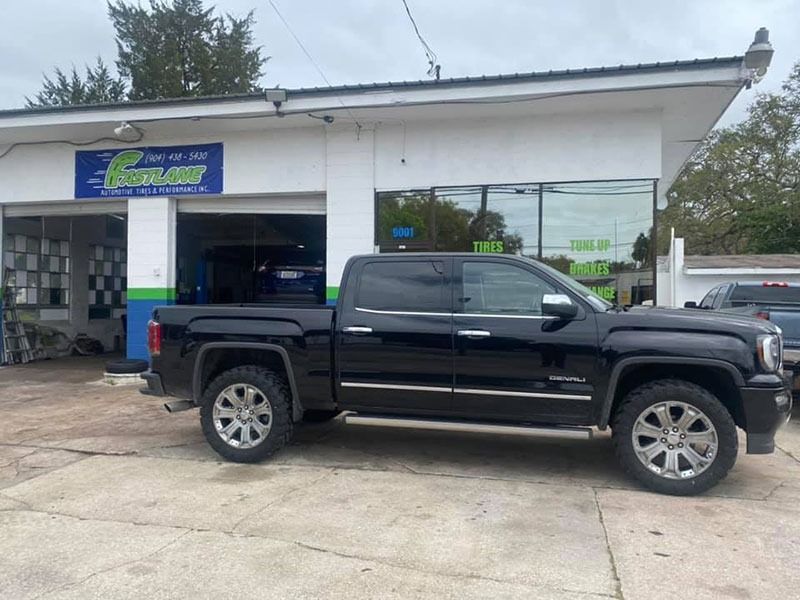 Black pickup truck parked outside a small auto shop with an open garage bay.