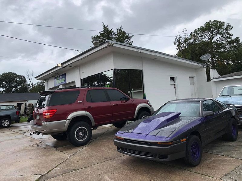 Maroon SUV and black sports car parked outside a white building on a cloudy day