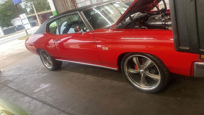 Red classic muscle car in a garage, hood open, with shiny chrome wheels.