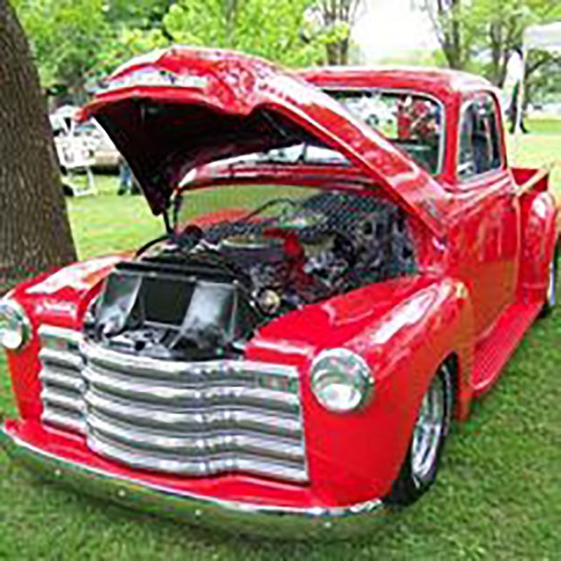 Bright red classic pickup truck with hood open, parked on grass outdoors