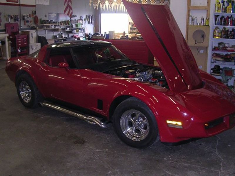 Red sports car with hood open inside a garage, showing the engine bay.