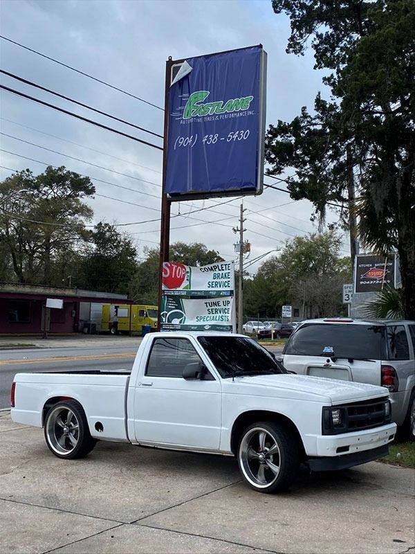 White lowered pickup truck parked beside a roadside sign under a cloudy sky