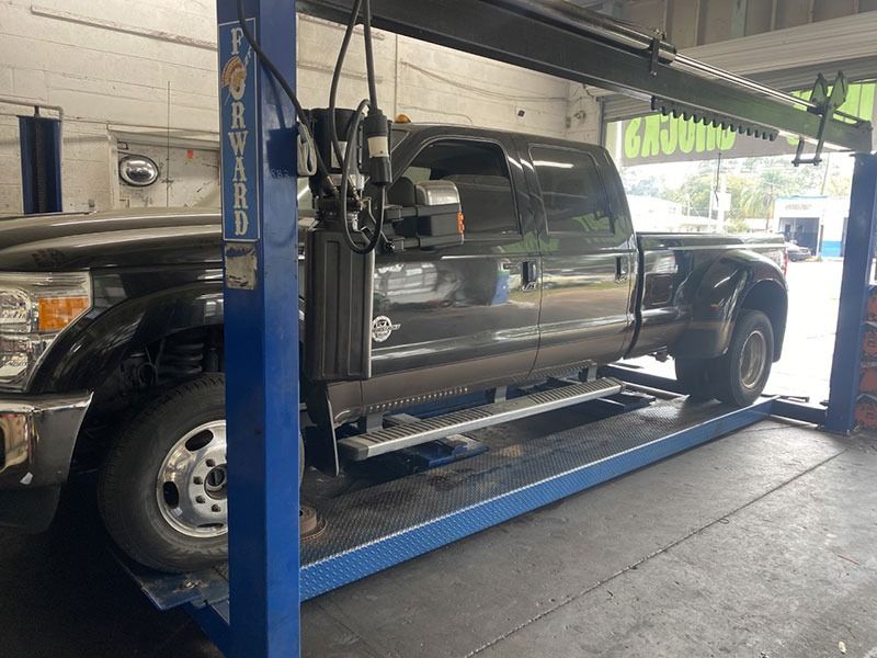 Black pickup truck on a blue hydraulic lift inside an auto repair shop