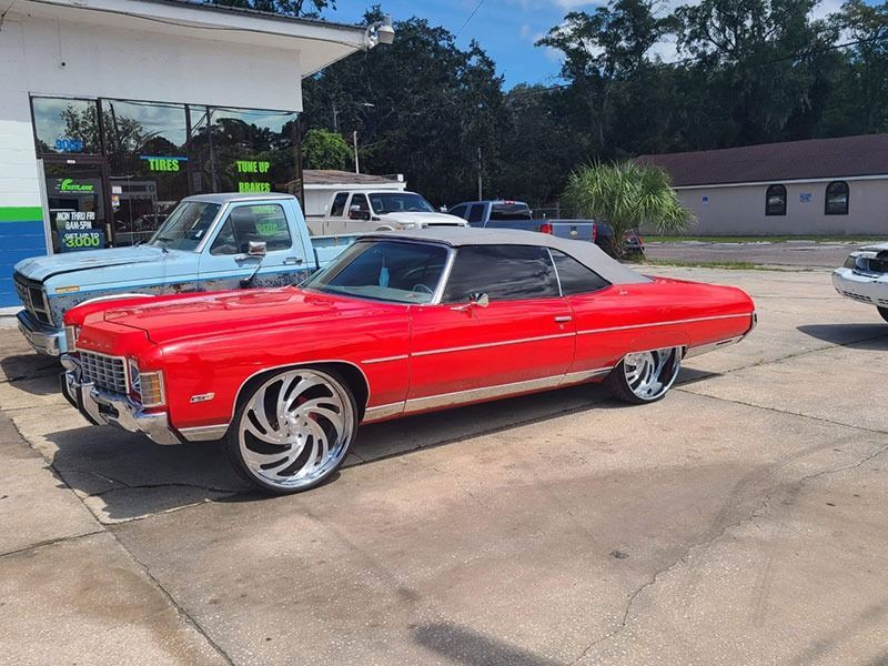 Red classic convertible car with oversized chrome wheels parked at a gas station