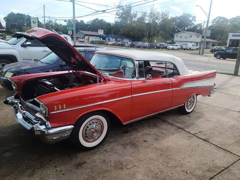 Red classic car with hood open at an outdoor lot, showing whitewall tires and chrome trim