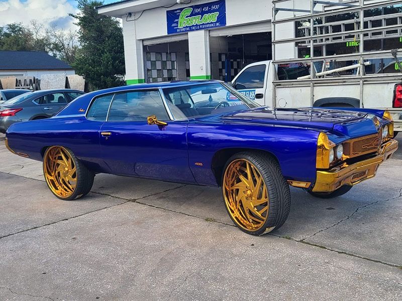 Blue classic car with gold rims parked outside a shop