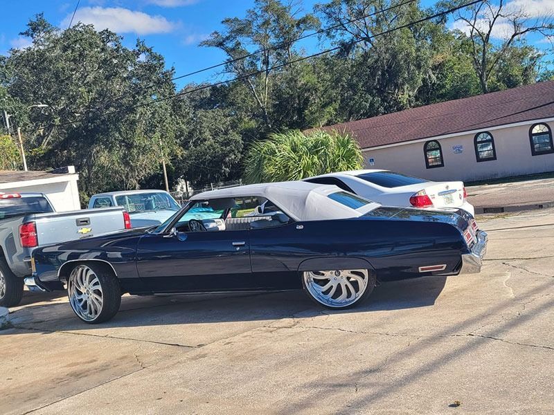 Black classic coupe parked outdoors beside a white car and building under a sunny sky