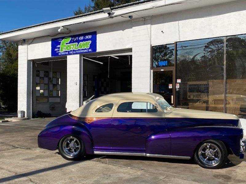 Purple classic car parked outside an auto shop.