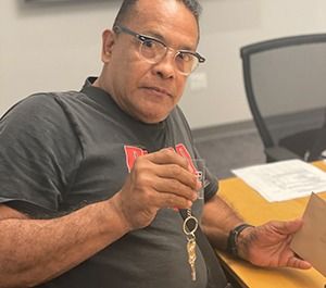 Man holding keys and envelope, sitting at a desk with glasses.
