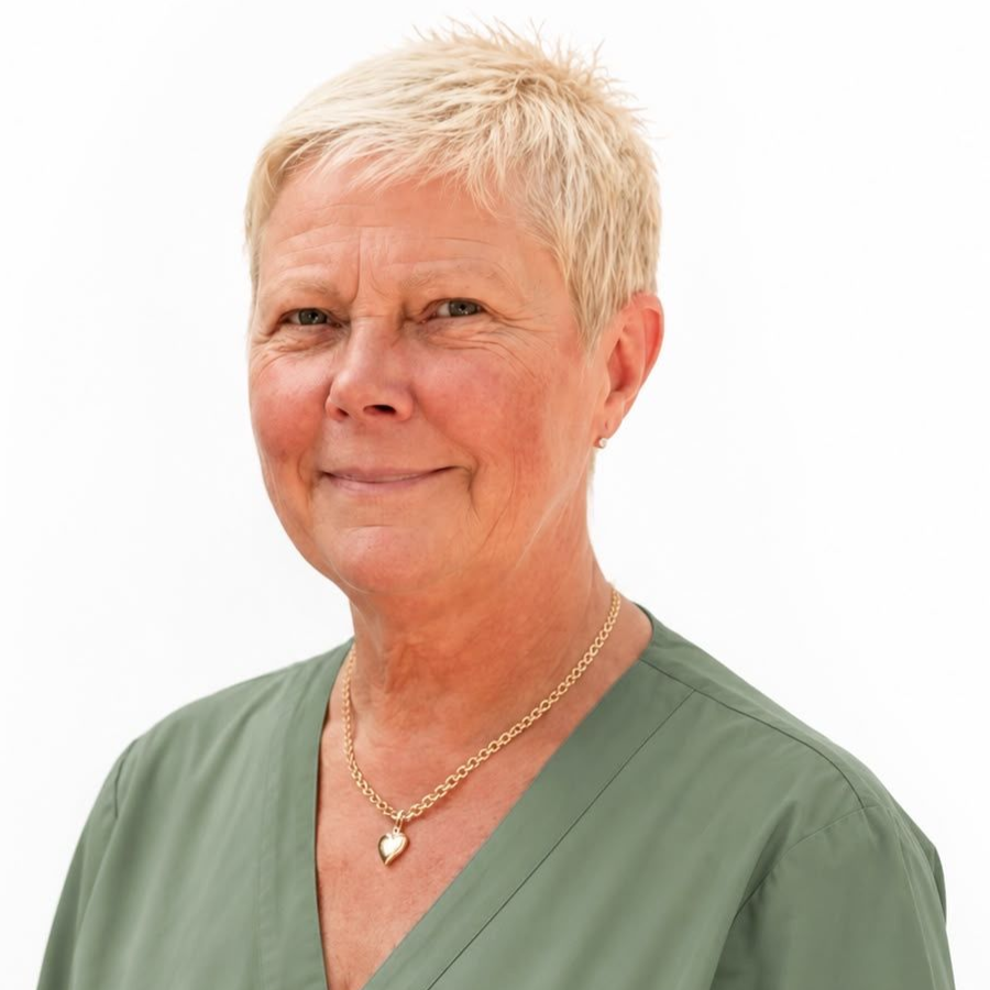 Porträtt av en person med kort blont hår som bär en grön V-ringad topp och ett guldhalsband mot en vit bakgrund