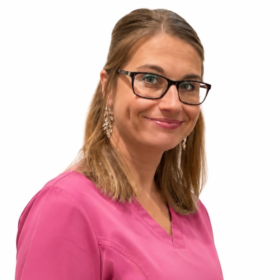 Kvinna i rosa scrubs och glasögon ler mot kameran mot en vit bakgrund