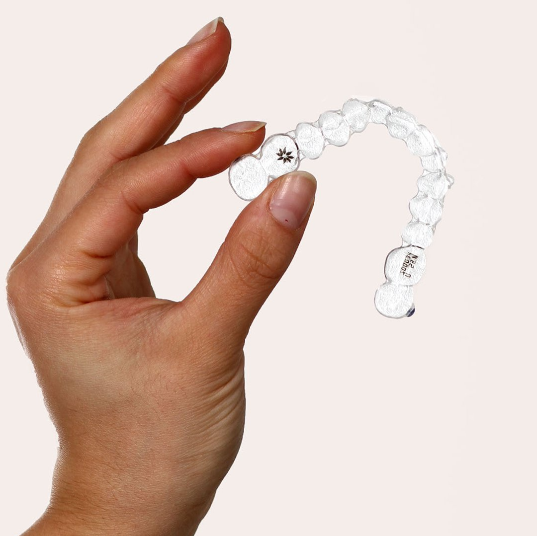 Hand som håller en genomskinlig tandhållare av plast, troligen för tänderutjämning.