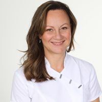 Leende kvinna med brunt hår, klädd i vit uniform, mot en vit bakgrund.