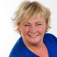 Leende blond kvinna i en blå topp mot en vit bakgrund