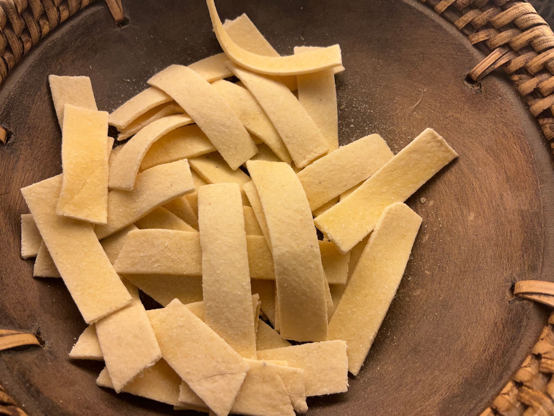Strisce di pasta in una ciotola di legno con bordo di vimini.