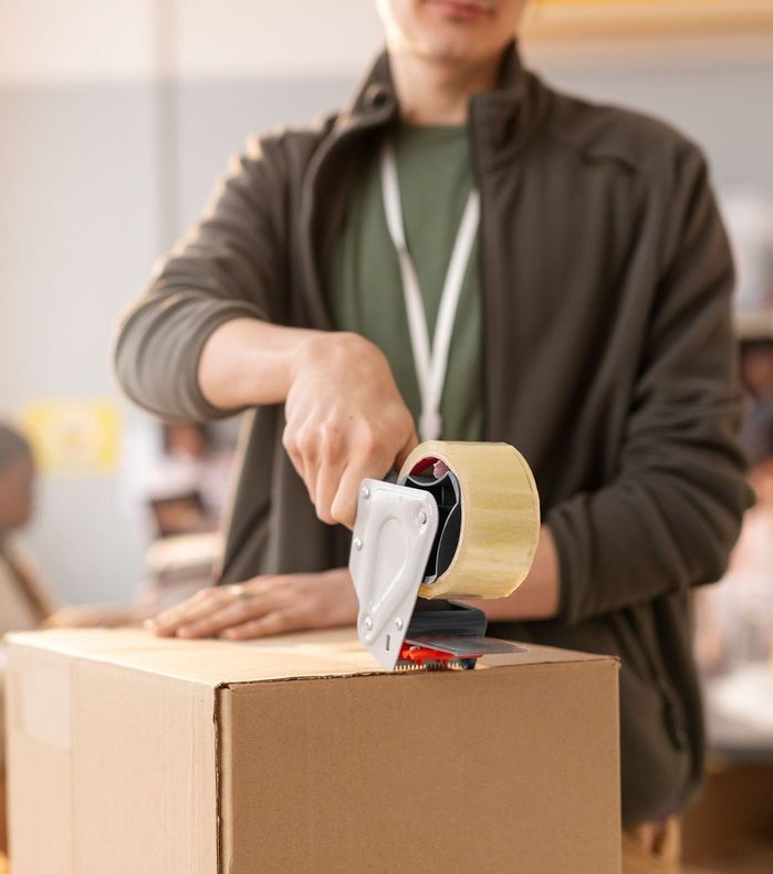 Um homem está colando uma caixa de papelão com fita adesiva