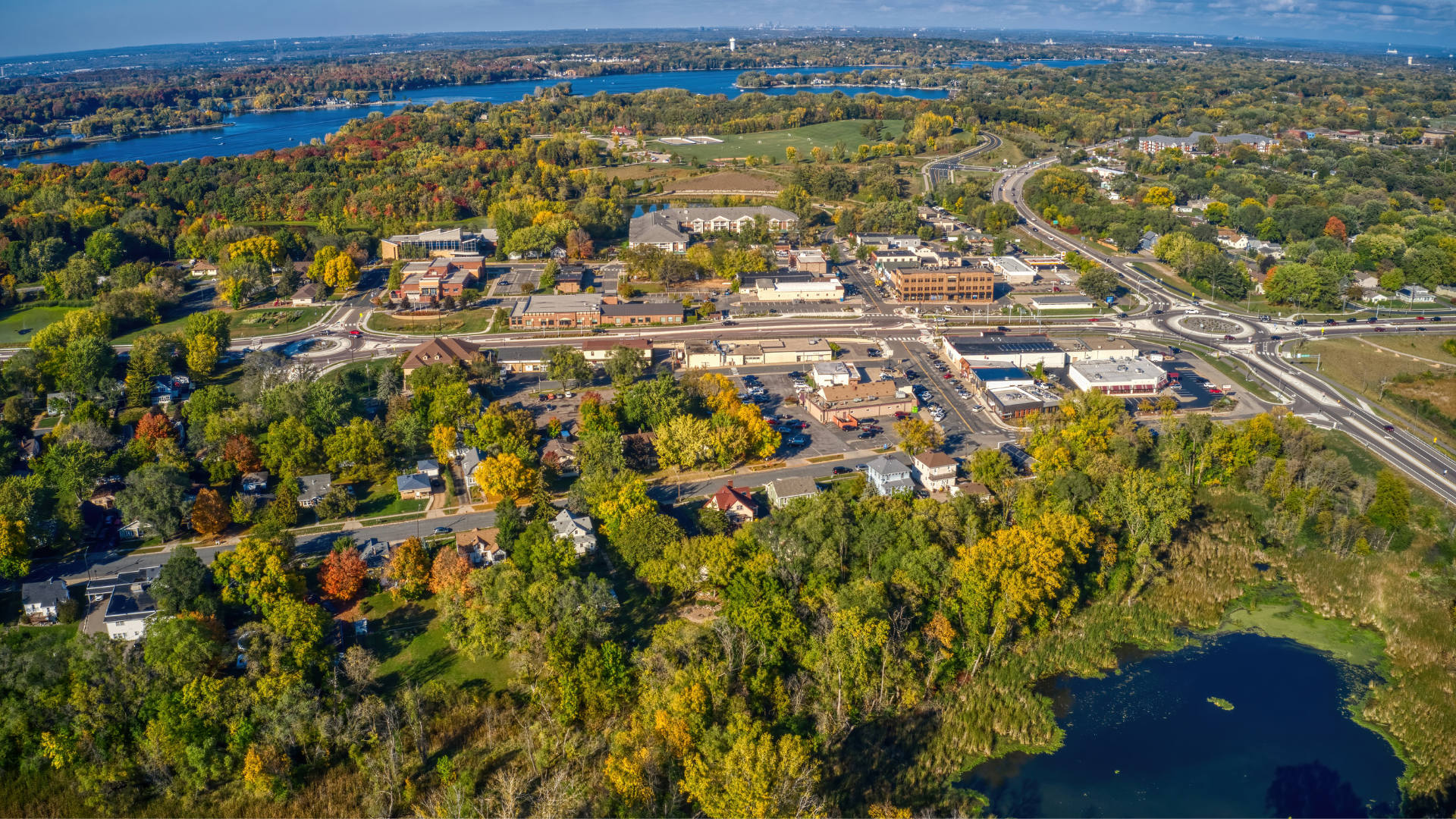 Aerial view of a small town with roads, trees, homes, and a lake in the distance.