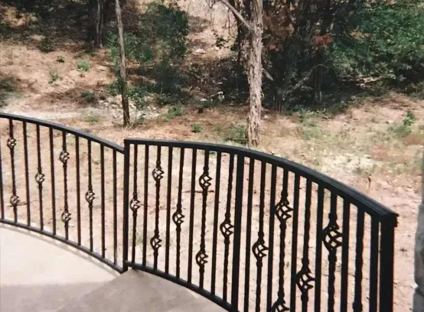 A wrought iron railing on a balcony with trees in the background