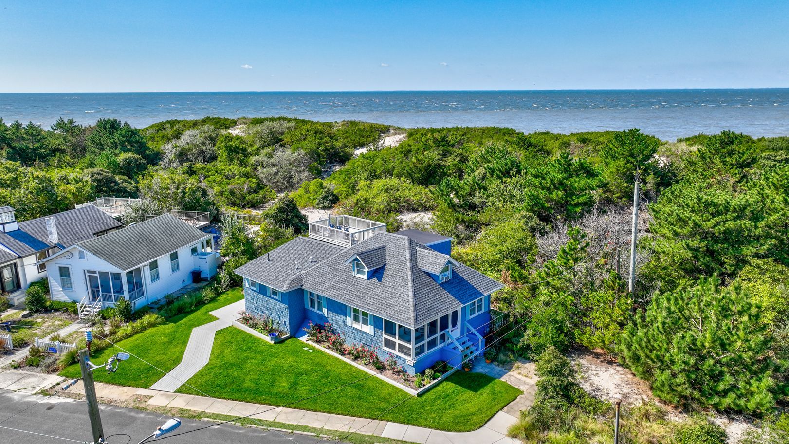 An aerial view of a blue house surrounded by trees next to the ocean.