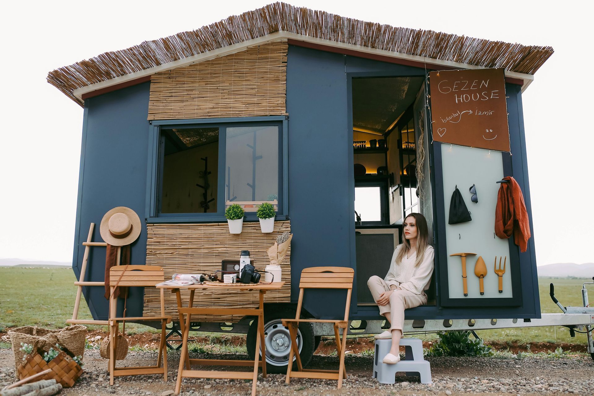 A woman is sitting on a stool in front of a small house.