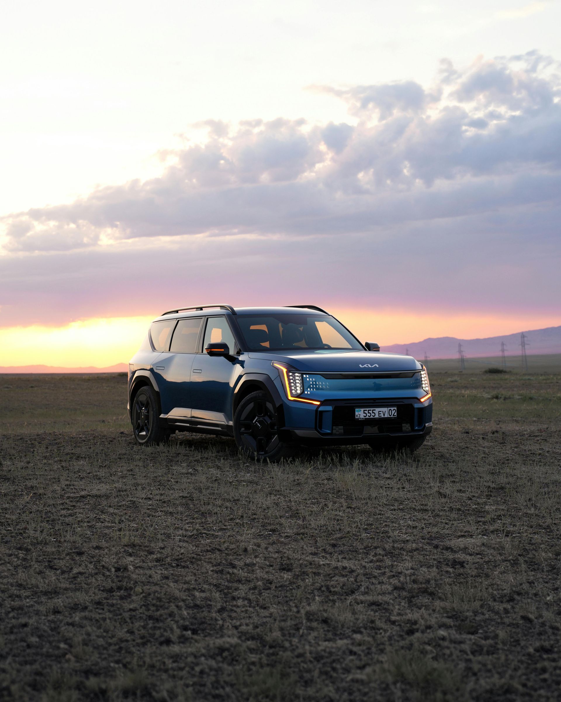 A blue suv is parked in a field at sunset.