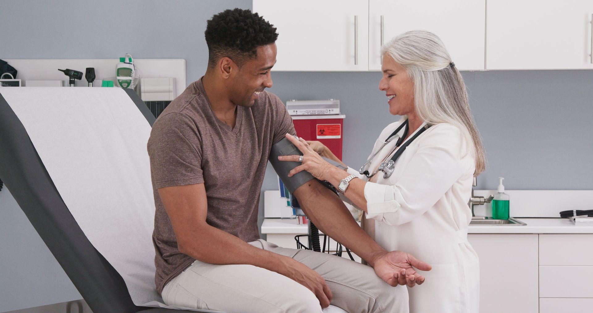 A patient seated in a room is having his blood pressure checked by a doctor at a medical clinic. A patient seated in a room is having his blood pressure checked by a doctor at a medical clinic.