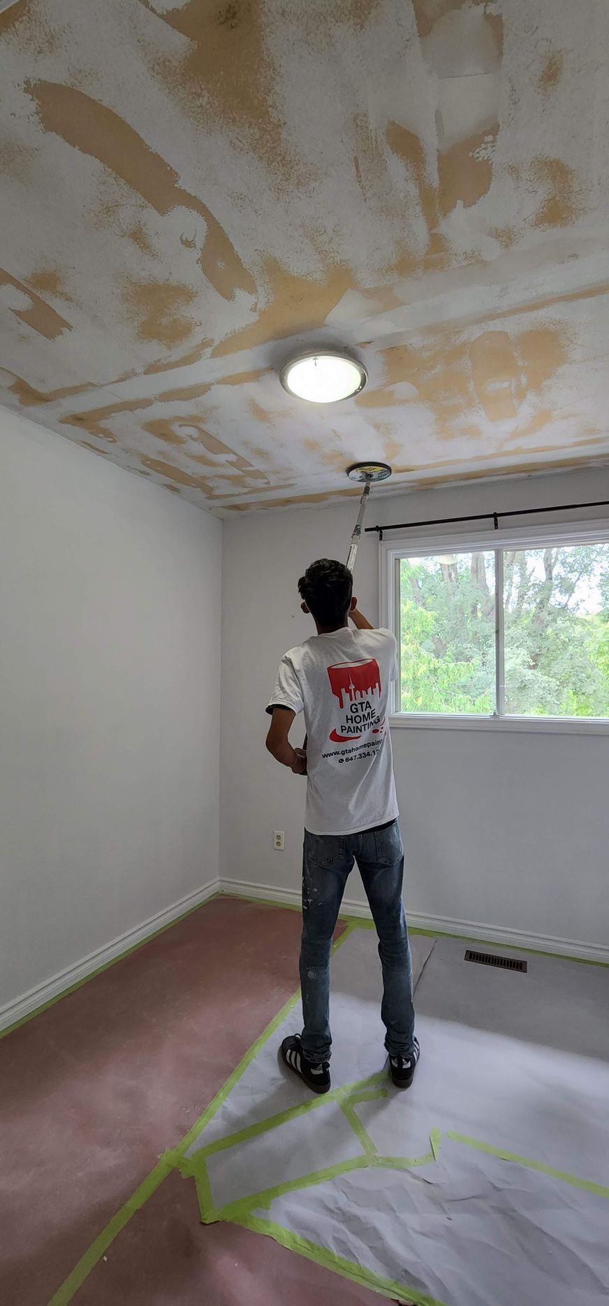 Worker on a tall ladder painting a vaulted white hallway with arched windows.