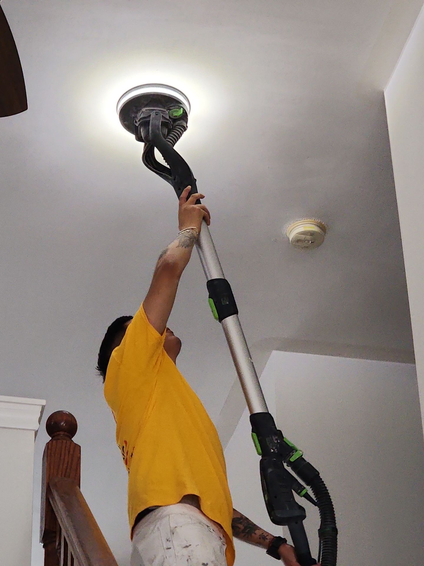 Person painting a ceiling light fixture with a roller while holding a brush, indoors.