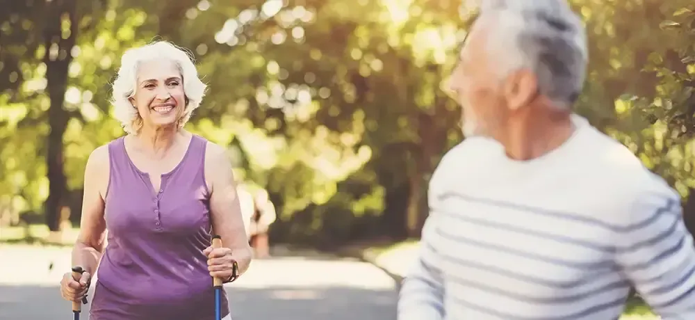 A man and a woman are walking in a park with nordic walking poles.