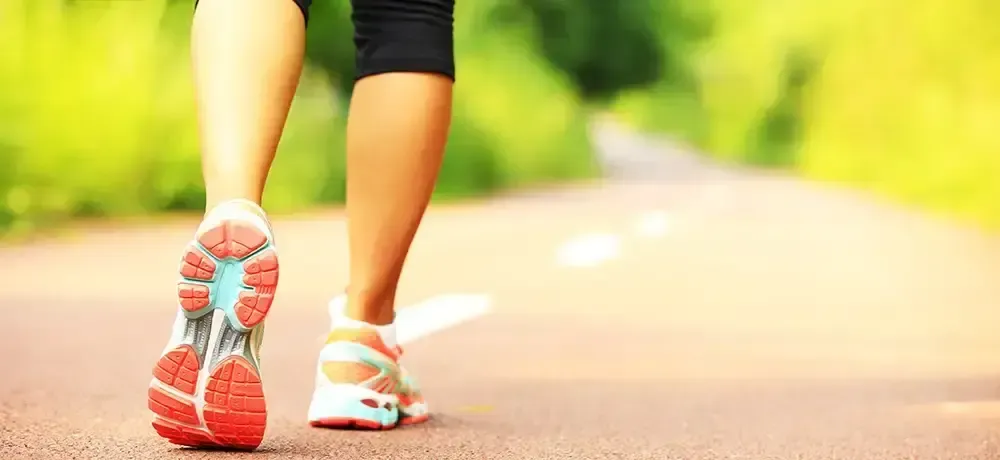 A woman is walking down a road wearing running shoes.