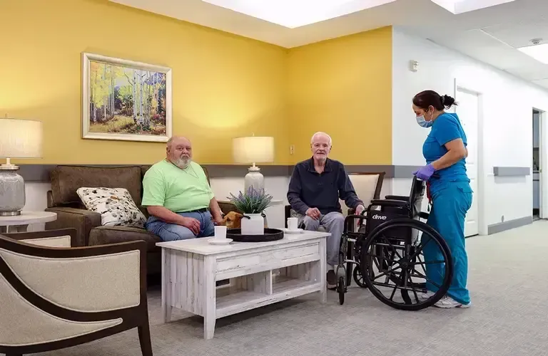 A man in a wheelchair is sitting in a living room with two other men.