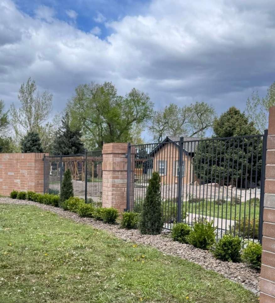 A brick fence surrounds a lush green yard with a house in the background.