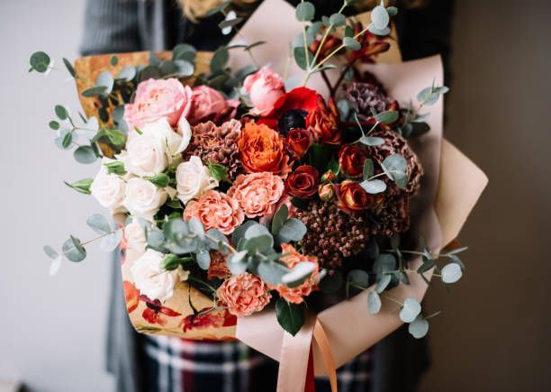 Bouquet of roses, eucalyptus, and other flowers wrapped in brown paper.