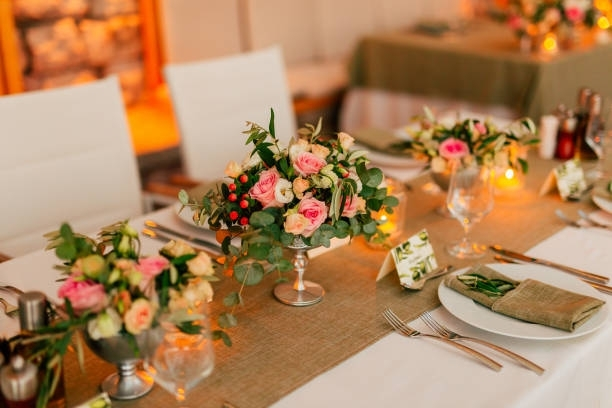 Wedding reception table setting with floral centerpieces, white chairs, and place settings.