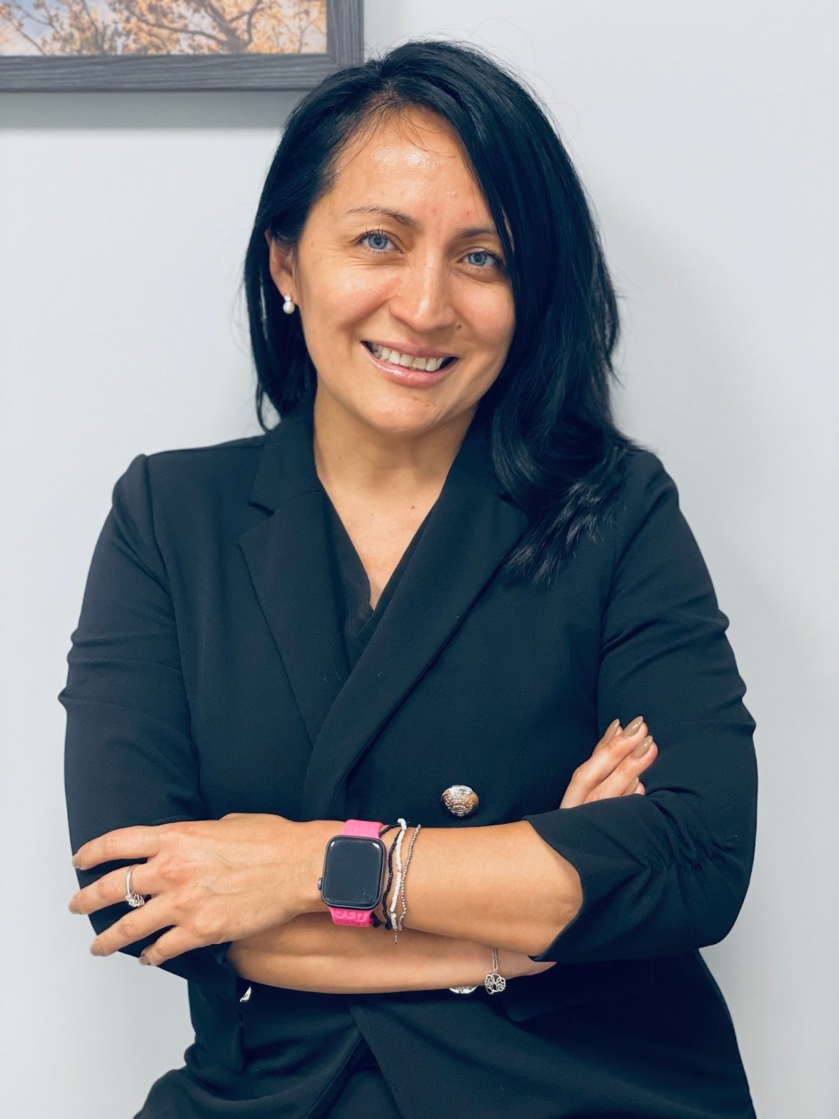 Woman with dark hair, wearing a black blazer, arms crossed, smiling.