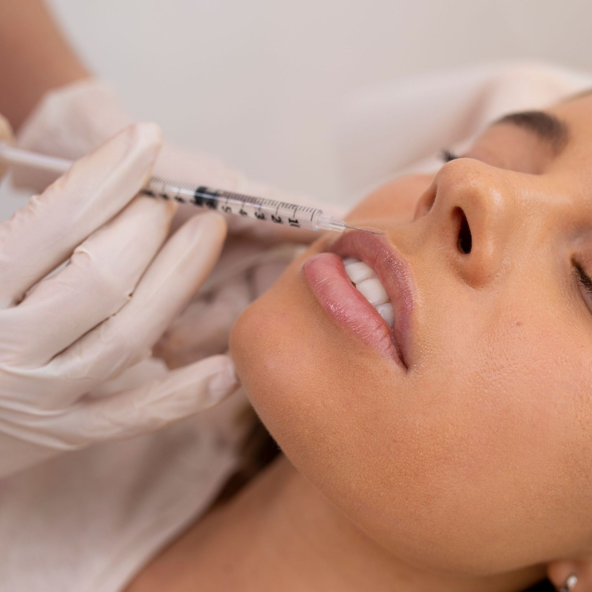 A person receiving lip injections. A gloved hand injects the person's lip.