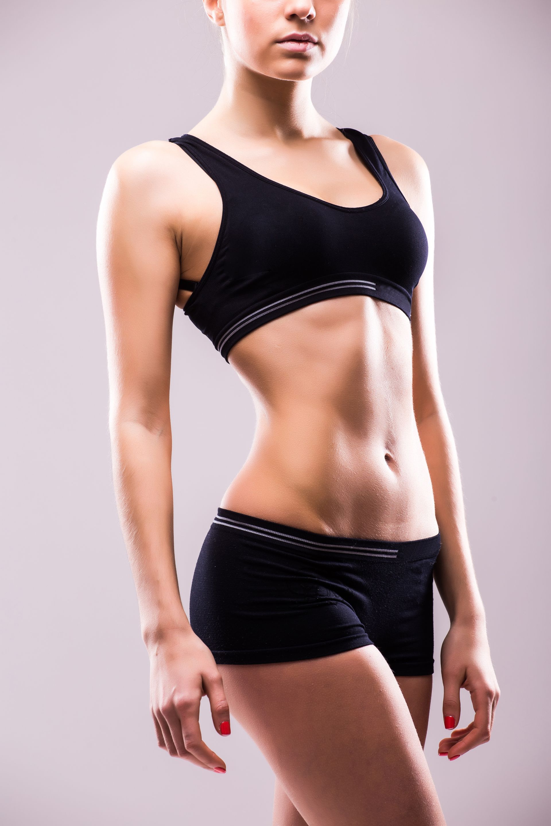 Woman in black workout clothes poses with a slim physique against a light background.