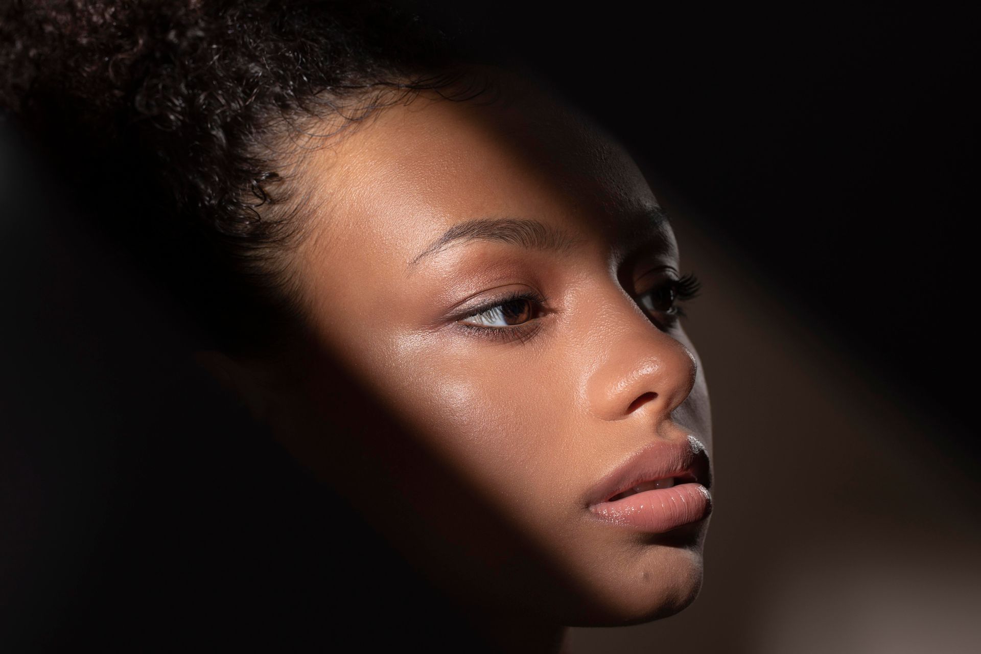 Woman's face in shadow and light. Highlights show dewy skin, defined nose and lips.