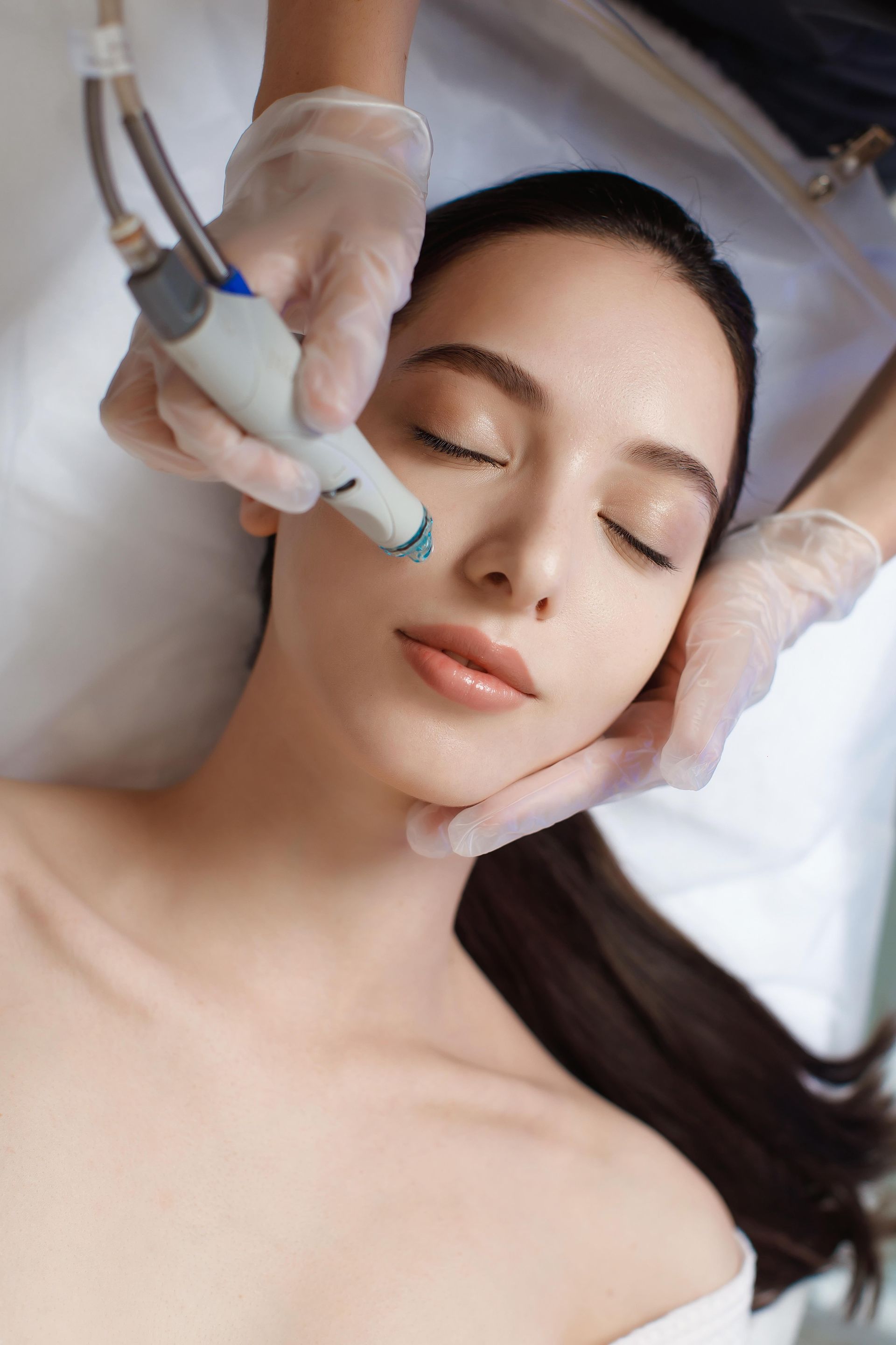 Woman receiving facial treatment with closed eyes, held by gloved hands.