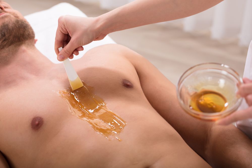 Person receiving chest waxing treatment. Technician applies wax with a spatula.