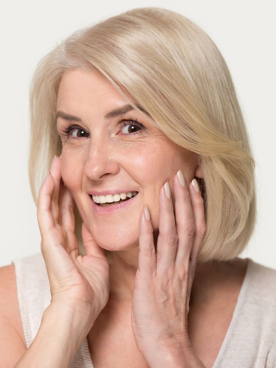 Woman with blonde hair smiling, touching her face with both hands.